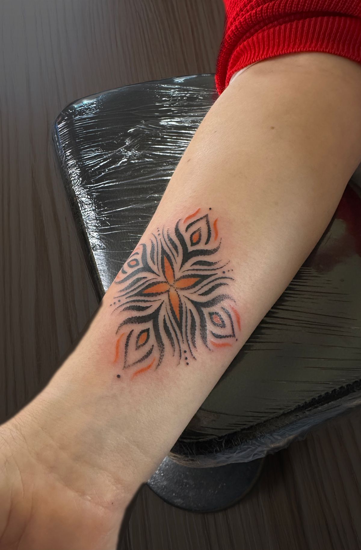 Tatouage vibratoire confiance en soi, fleur étoilée noire au cœur orange sur l'avant-bras